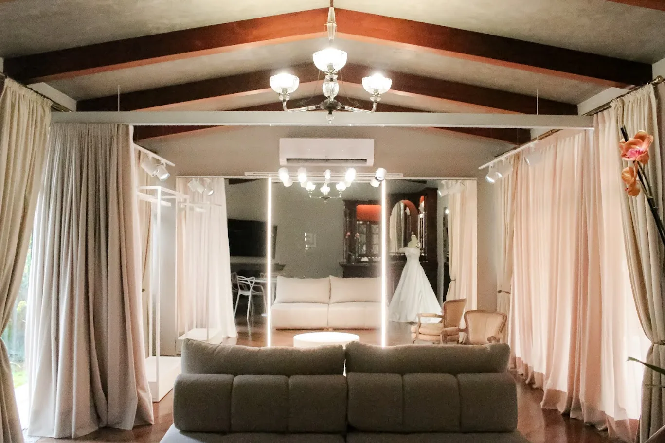 Salão da casa com vigas de madeira, lustre e cortinas de linho