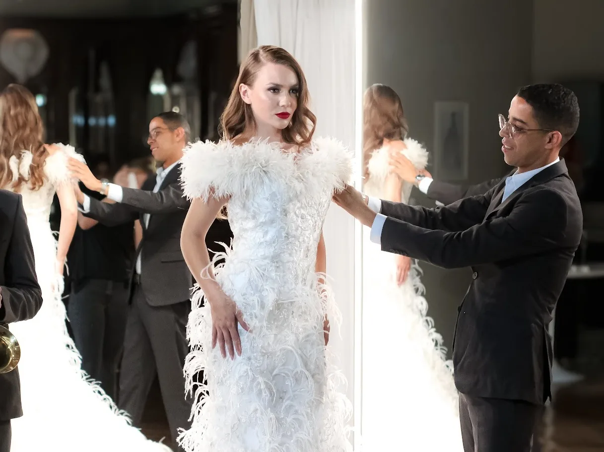 Leandro Fonseca ajustando a gola de plumas de um vestido, de perfil